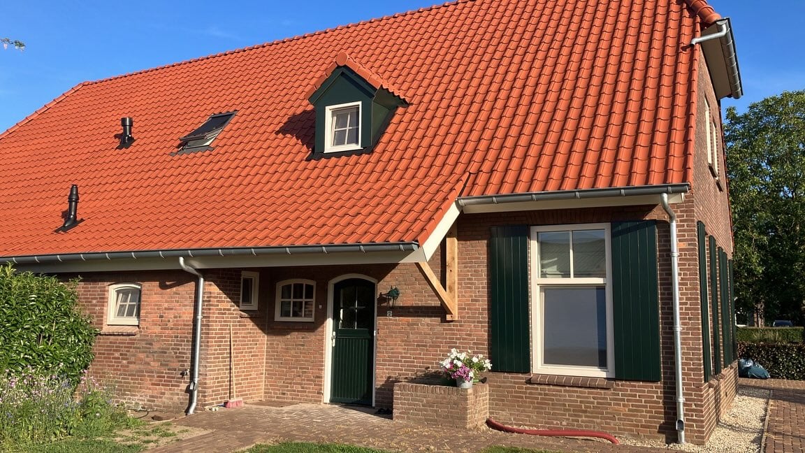 Boerderij in Mill na de gevelrenovatie: rode gevel, oranje pannendak, groene deur en luiken