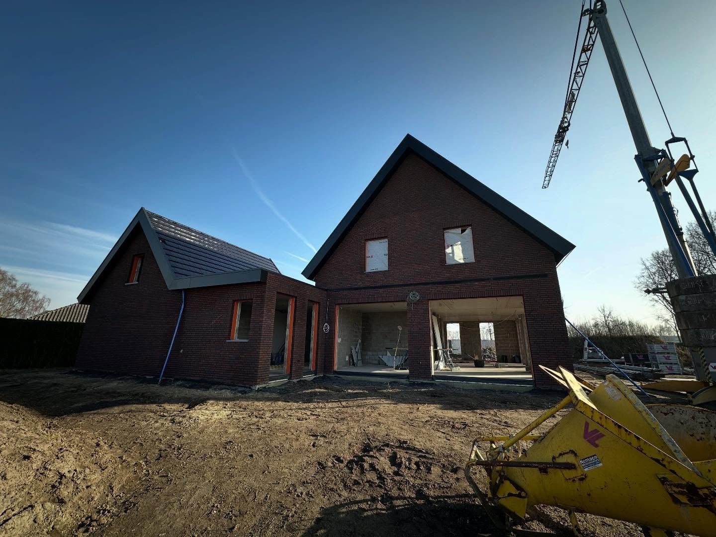 Nieuwbouwwoning met rood-bruine gevel en zwarte voeg, de bouwkraan nog ernaast